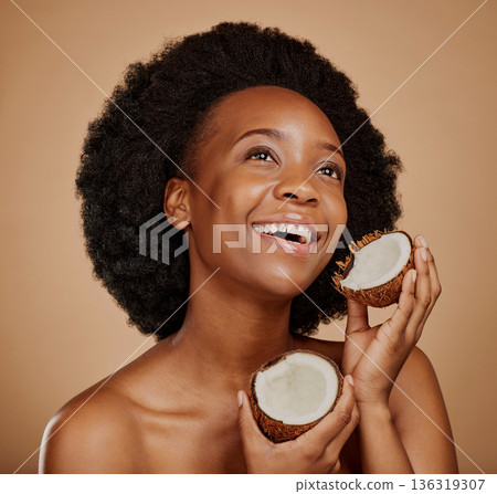 Beauty, skincare and coconut with a model black woman in studio on a brown background for natural treatment. Thinking, skin and cosmetics with a happy young female person holding fruit for oil Beauty, skincare and coconut with a model black woman in studio on a brown background for natural treatment. Thinking, skin and cosmetics with a happy young female person holding fruit for oil 136319307