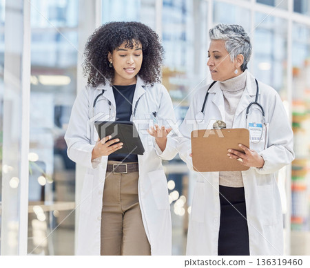 Team, tablet and documents with woman doctors walking in a hospital for insurance or healthcare discussion. Collaboration, trust and consulting with female medicine professionals talking in a clinic 136319460