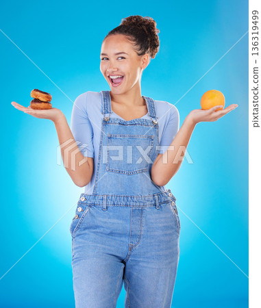 Portrait, excited and woman with donut, orange and choice in studio isolated on blue background. Happy, fruit or person with doughnut, fast food or comparison for healthy diet, nutrition or wellness 136319499