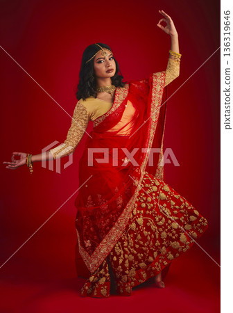 Portrait, dance and Indian woman with traditional dress, celebration and motion against a red studio background. Face, female person and model with cultural clothes, jewellery and dancing with ritual 136319646