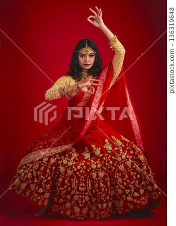 Portrait, dance and Indian woman with fashion, traditional dress and celebration against a red studio background. Face, female person or model with cultural clothes, jewellery and dancing with beauty Portrait, dance and Indian woman with fashion, traditional dress and celebration against a red studio background. Face, female person or model with cultural clothes, jewellery and dancing with beauty 136319648