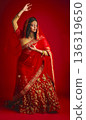Fashion, dancing and Indian woman in a traditional dress, celebration and confident on a red studio background. Female person, girl and model with a cultural outfit, dancer and ritual with confidence 136319650