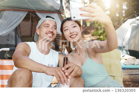 Selfie, love and young couple on a camp in the woods for a summer weekend trip or holiday. Happy, smile and man with beer while his girlfriend taking a picture in forest on outdoor vacation together. 136320305