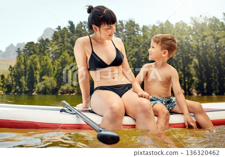 Lake, woman and boy child on paddle board, relax outdoor with summer holiday and travel. Adventure, freedom with mother and son in swimsuit with feet in water, vacation and family bonding together Lake, woman and boy child on paddle board, relax outdoor with summer holiday and travel. Adventure, freedom with mother and son in swimsuit with feet in water, vacation and family bonding together 136320462