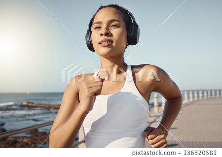 Fitness, woman run at beach and with headphones listening to music for training. Exercise or marathon, lens flare or sportswear and female athlete running along the promenade listen to radio Fitness, woman run at beach and with headphones listening to music for training. Exercise or marathon, lens flare or sportswear and female athlete running along the promenade listen to radio 136320581