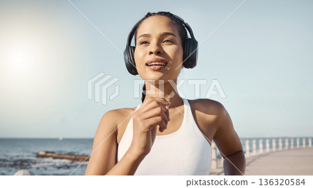 Fitness, woman and running at seaside with headphones for exercise with wellness, audio and sunshine. Girl, listening and music with workout at ocean in summer for cardio or healthy body in morning. Fitness, woman and running at seaside with headphones for exercise with wellness, audio and sunshine. Girl, listening and music with workout at ocean in summer for cardio or healthy body in morning. 136320584