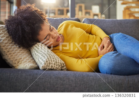 Stomach pain, sick and menstruation with woman on sofa for healthcare, endometriosis and tired. Digestion, medical and constipation with person in living room at home for nausea, virus and fear 136320831