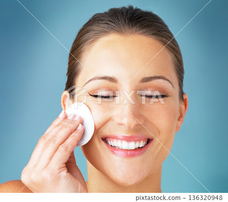 Skincare, portrait and happy woman with cotton pad on face, cosmetics and makeup cleaning product. Dermatology, skin care and wellness for model with beauty, smile and facial glow on blue background. Skincare, portrait and happy woman with cotton pad on face, cosmetics and makeup cleaning product. Dermatology, skin care and wellness for model with beauty, smile and facial glow on blue background. 136320948