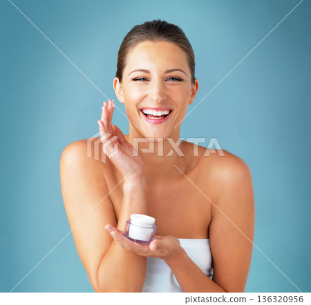 Skincare, dermatology and portrait of happy woman with cream, cosmetics and product on blue background. Lotion, skin care and wellness, model with smile, beauty treatment and facial glow in studio. Skincare, dermatology and portrait of happy woman with cream, cosmetics and product on blue background. Lotion, skin care and wellness, model with smile, beauty treatment and facial glow in studio. 136320956