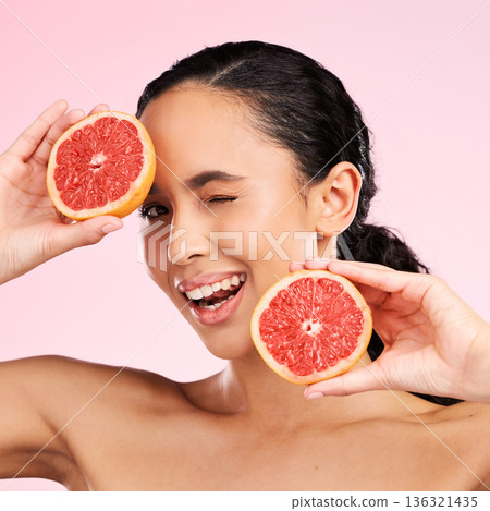 Face, beauty and woman wink with grapefruit in studio isolated on a pink background. Portrait, natural cosmetic and model with fruit, food or nutrition for skincare, healthy vegan diet or vitamin c Face, beauty and woman wink with grapefruit in studio isolated on a pink background. Portrait, natural cosmetic and model with fruit, food or nutrition for skincare, healthy vegan diet or vitamin c 136321435