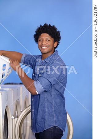 Laundry, portrait of a black man at washing machine and basket at laundromat with a smile. Hygiene, service and African male person cleaning clothes for health wellness or protection from bacteria 136321797