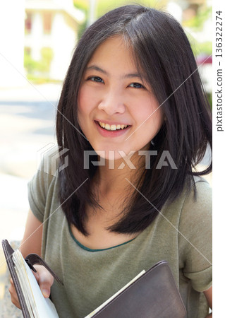 Portrait, education and book with an asian woman student on university campus for learning or development. Study, smile or happy with a young female college pupil outdoor to study or learn in summer Portrait, education and book with an asian woman student on university campus for learning or development. Study, smile or happy with a young female college pupil outdoor to study or learn in summer 136322274