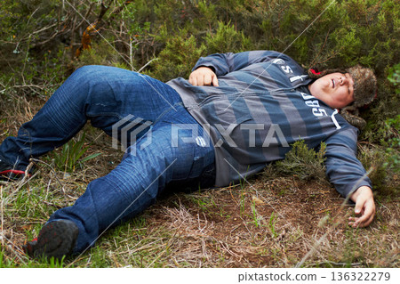Drunk, sleeping and hangover with a plus size man lying outdoor on the grass or ground after a party. Festival, alcohol and tired with a young male person asleep on a field or lawn in the morning 136322279
