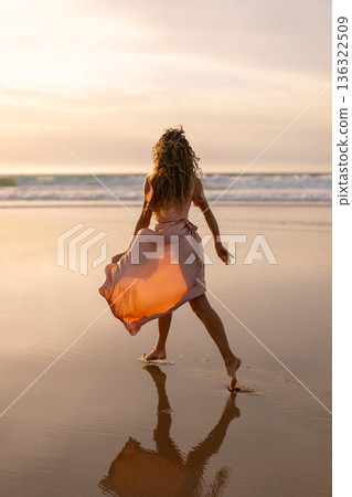 Woman in flowing dress walking barefoot on beach 136322509