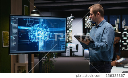 Manager in office using screen to analyze machine learning algorithms built by workers. Startup team leader supervising code written by employees to improve artificial intelligence Manager in office using screen to analyze machine learning algorithms built by workers. Startup team leader supervising code written by employees to improve artificial intelligence 136322867