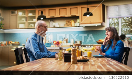 Senior wife looking exasperated and disengaged as husband continues talking, strained morning routine shows displeasure and monotony in domestic retired life together. Fed up person. Camera A. Senior wife looking exasperated and disengaged as husband continues talking, strained morning routine shows displeasure and monotony in domestic retired life together. Fed up person. Camera A. 136322910