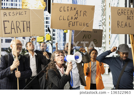 Senior woman with loudspeaker and activists marching in a climate protest with banners on the street for nature conservation. Protesting for global warming, ecology and activism. Senior woman with loudspeaker and activists marching in a climate protest with banners on the street for nature conservation. Protesting for global warming, ecology and activism. 136322963
