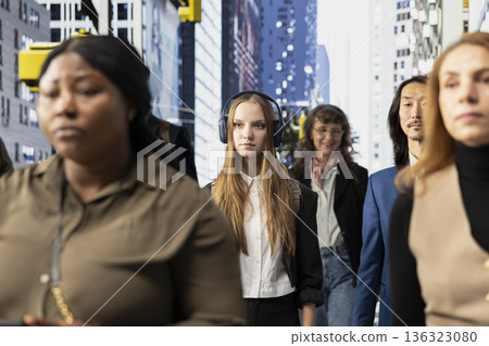 Lively group of female and male pedestrians walking through a business district, showing vibrant motion of urban crowd culture with people engaged in routine and city street activity. 136323080