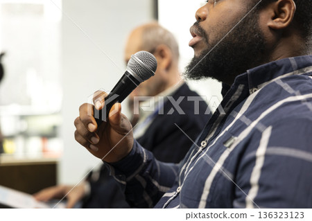 African american participant engaging and interacting during presentation, asking questions on microphone. Corporate business meeting with panel discussion and speaker, international conference. 136323123