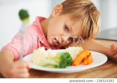 Sad, healthy and a child with vegetables for dinner, unhappy and problem with food. Frustrated, hungry and a little boy eating broccoli and carrots, disappointed with lunch and nutrition for youth 136323261