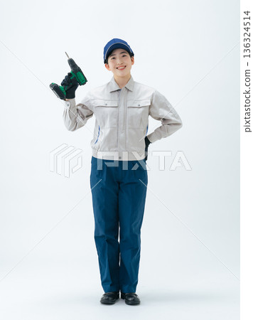 一位身穿工作服的女性手持電動螺絲起子的全身照 一位身穿工作服的女性手持電動螺絲起子的全身照 136324514
