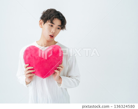 Portrait of a young man holding a heart cushion Portrait of a young man holding a heart cushion 136324580