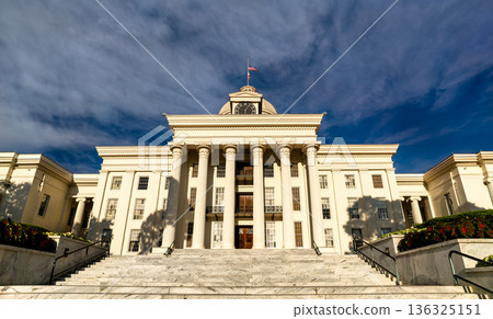 Alabama State Capitol in Montgomery, United States. Greek Revival architecture features a white portico, columns and grand marble staircase under a blue sky 136325151