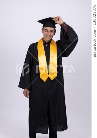 Proud graduate student holding diploma and adjusting cap 136325376