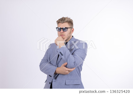 Man in grey suit and sunglasses thinking with hand on chin 136325420