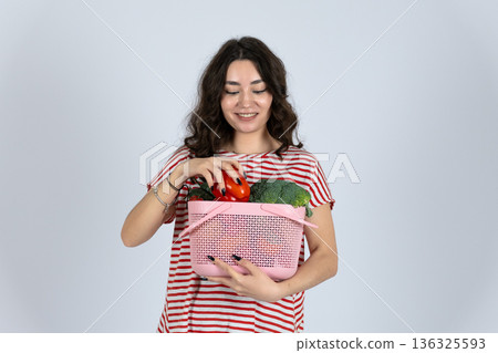Happy woman holding basket with fresh vegetables and pepper Happy woman holding basket with fresh vegetables and pepper 136325593