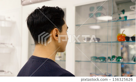 Man looking at the wall of glasses in shop Man looking at the wall of glasses in shop 136325626