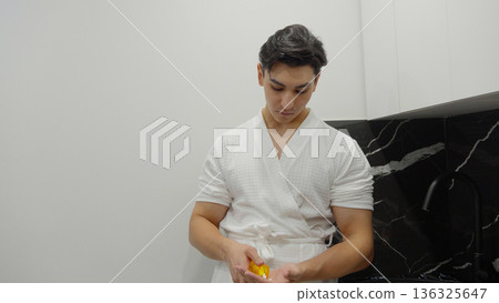 Young man sitting in kitchen and using smartphone Young man sitting in kitchen and using smartphone 136325647
