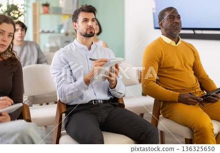 Students of different ages listen attentively to teacher and take notes in notebooks during a lecture at the learning center. Language course Students of different ages listen attentively to teacher and take notes in notebooks during a lecture at the learning center. Language course 136325650
