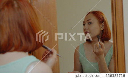 Woman applying makeup while looking in the mirror Woman applying makeup while looking in the mirror 136325736