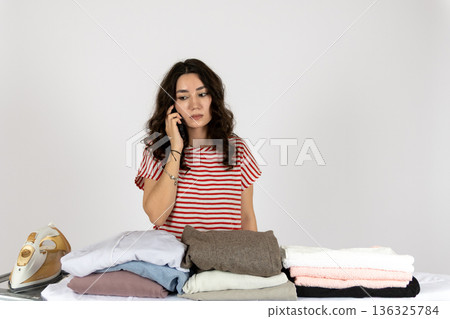 Housewife talking on phone while holding fresh laundry Housewife talking on phone while holding fresh laundry 136325784