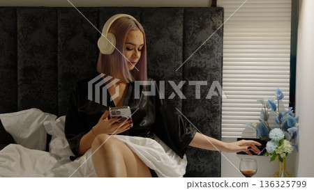 Woman relaxing on bed and using her smartphone Woman relaxing on bed and using her smartphone 136325799