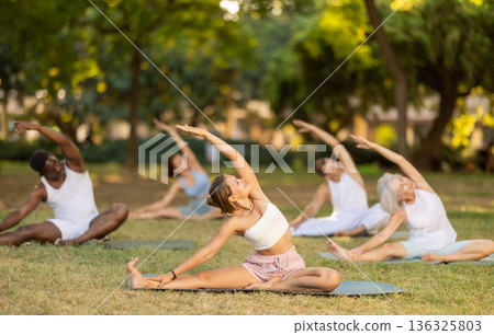 Girl stretching in Janu Sirsasana during group yoga in park Girl stretching in Janu Sirsasana during group yoga in park 136325803