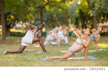 Girl performing Parivrtta Anjaneyasana in group yoga class outdoors 136325851
