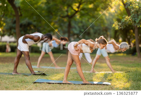 Girl performing Pyramid Pose during group young class in park Girl performing Pyramid Pose during group young class in park 136325877