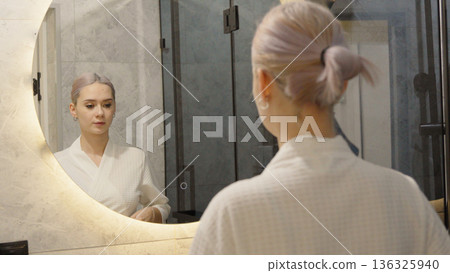 Woman looking in the mirror and touching her hair Woman looking in the mirror and touching her hair 136325940