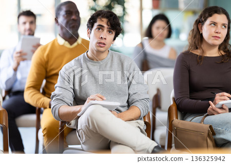 Young man listens and takes notes in lecture hall Young man listens and takes notes in lecture hall 136325942