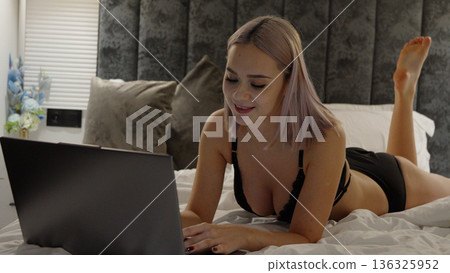 Woman lying in bed and working on a laptop 136325952