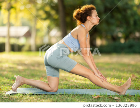 Slim woman practicing yoga - virabhadrasana pose in summer park Slim woman practicing yoga - virabhadrasana pose in summer park 136325996