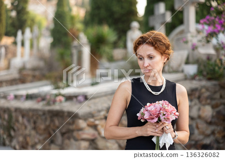 Woman in mourning black dress standing in cemetery with flowers Woman in mourning black dress standing in cemetery with flowers 136326082