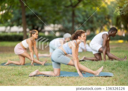 Woman performing Ardha Hanumanasana in group yoga class in park 136326126