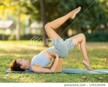 Woman leading an active lifestyle, training in a summer park, performing dynamic asanas to improve body flexibility 136326406