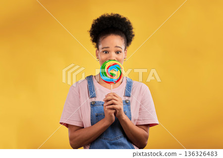 Portrait, black woman with candy or lollipop in studio on yellow background and eating sweets, dessert or food with sugar. Gen z, face of girl and hungry for delicious treats, snack or product 136326483