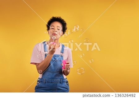 Blowing bubbles, woman and fun in studio while playful for birthday or party celebration. Black female model person with liquid soap, natural beauty and fashion on a yellow background with space Blowing bubbles, woman and fun in studio while playful for birthday or party celebration. Black female model person with liquid soap, natural beauty and fashion on a yellow background with space 136326492