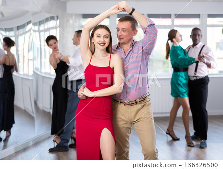 Man and woman in elegant clothes performing ballroom dance in dancing room during celebration or party 136326500