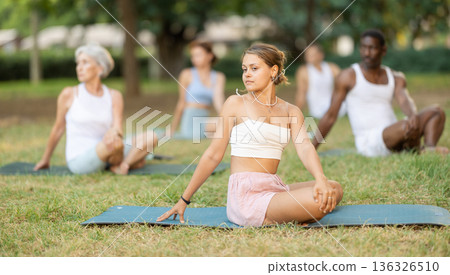 Multinational yoga enthusiasts with female coach perform padmasana in park Multinational yoga enthusiasts with female coach perform padmasana in park 136326510